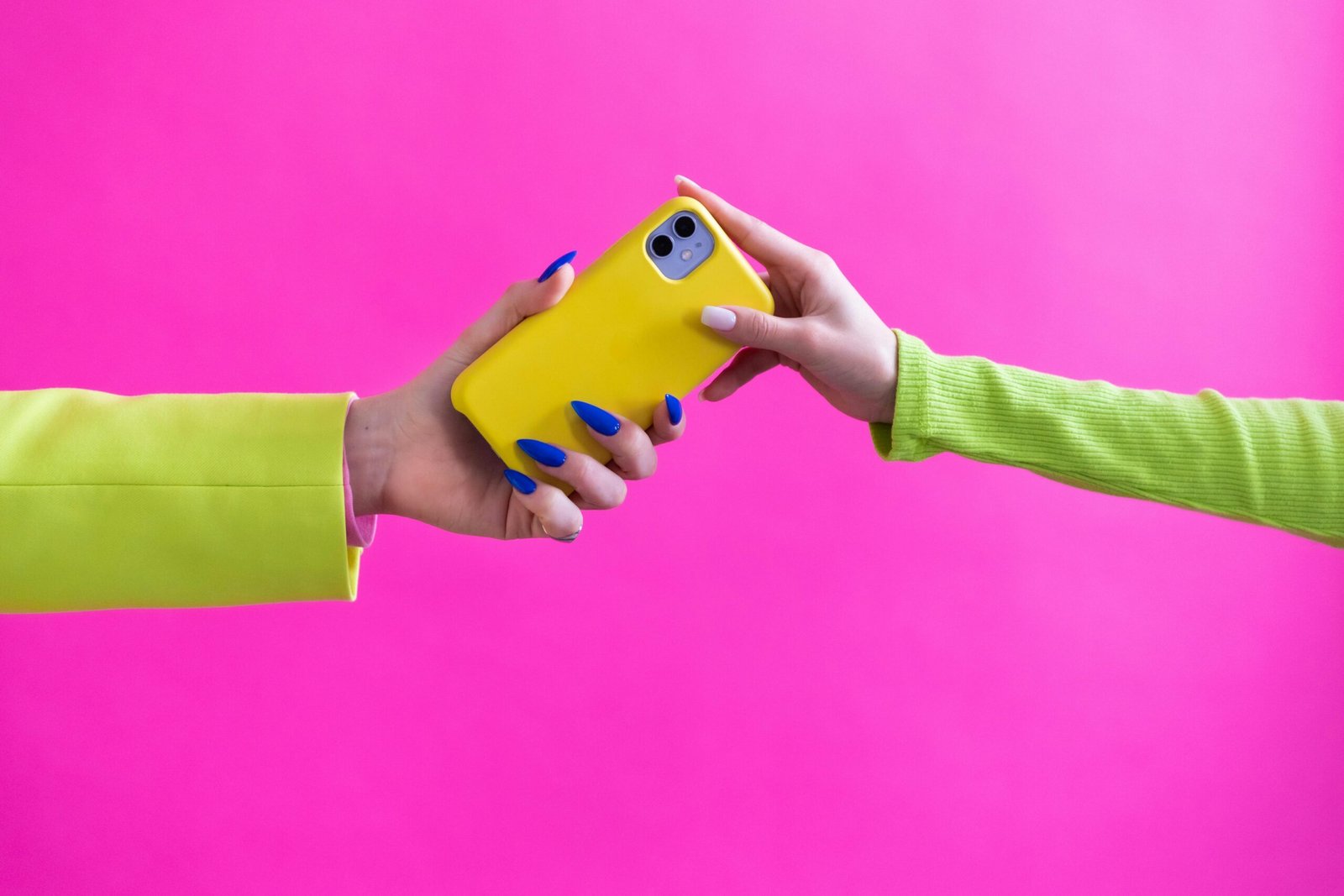 Colorful studio image of hands exchanging a yellow smartphone against a pink backdrop.